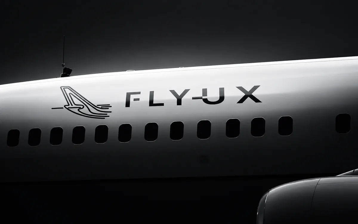 FlyUX livery: the FlyUX wordmark and bird mark on the white fuselage of an aircraft, lit against black
